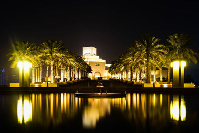 Illuminated building by lake against sky at night