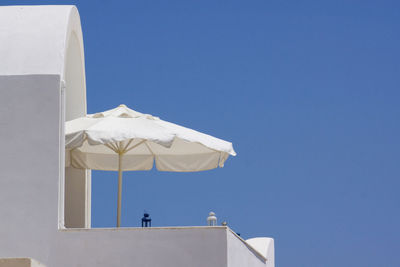 Low angle view of umbrella at balcony of building against clear blue sky