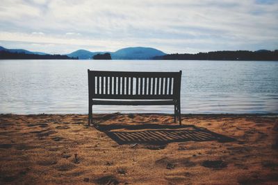 Empty bench on beach against sky and water