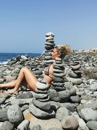 Stack of stones on rock by sea against clear sky