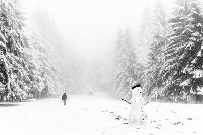 Snowman on field amidst pine trees