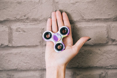 Close-up of woman hand holding fidget spinner against wall