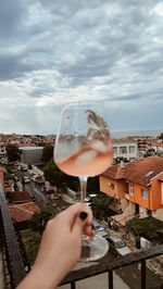 Cropped hand of woman holding drink against sky