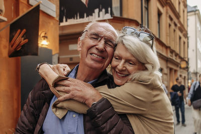 Happy senior woman hugging man from behind in city