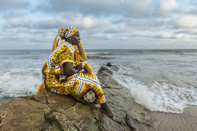 African woman with long dress sitting on stone cliff after the coast in accra ghana west africa