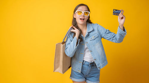 Portrait of smiling young woman standing against yellow background