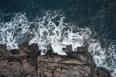 Drone view of foamy blue sea waving on rocky shoreline with rough boulders