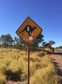 Road sign on field against clear blue sky