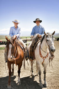 Portrait of man and woman sitting on horses in ranch against sky