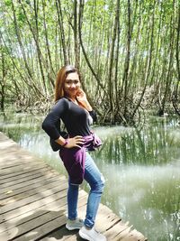 Portrait of woman standing by lake against trees