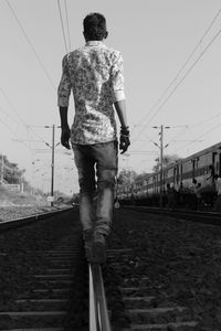 Rear view of man standing on railroad track against sky