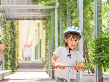 Little boy rides kick scooter in skate park. kid in helmet. training to skate at summer.