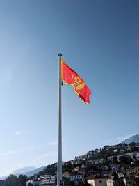 Low angle view of flag against buildings against clear blue sky