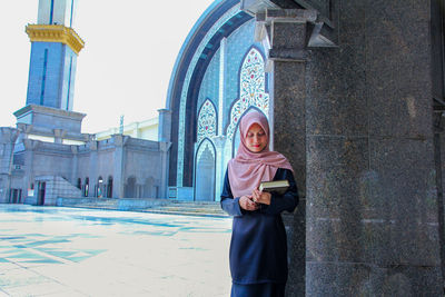 Woman holding holy book while standing outside mosque