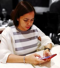 Close-up of woman using mobile phone while sitting by table indoors