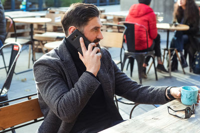 Brutal bearded middle-aged man in a street cafe talking on a mobile phone