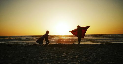 Silhouette people standing on beach against clear sky during sunset