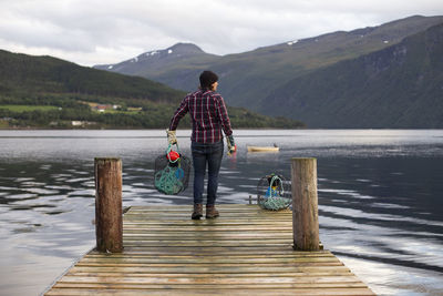 Rear view of man standing on lake against mountains