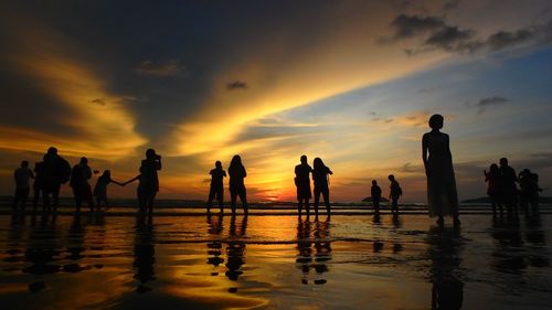 Silhouette people at beach against cloudy sky during sunset