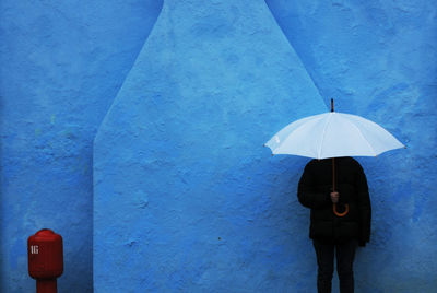 Boy with white umbrella standing against blue wall