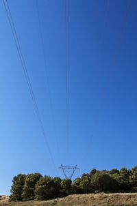 Low angle view of power lines against clear blue sky