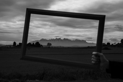 Cropped hand holding picture frame against sky