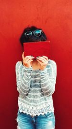 Woman with face covered by book against red background
