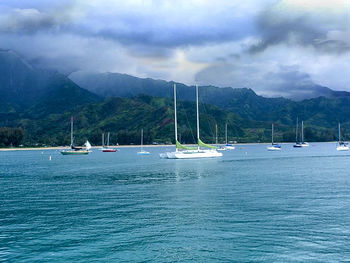 Sailboats in sea against cloudy sky