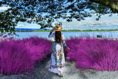 Rear view of woman standing on pink flowering plants against sky