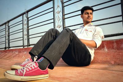 Young man sitting on building terrace against sky