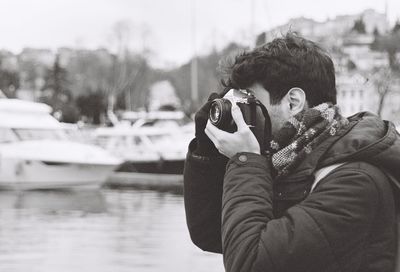 Portrait of man photographing by lake during winter