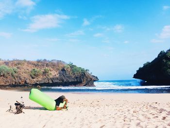 Man sitting on beach against blue sky