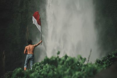 Rear view of shirtless man standing in forest with indonesian national flag