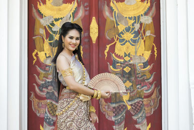 Portrait of smiling teenage girl wearing traditional clothing standing against door