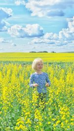 Smiling girl standing amidst yellow flowering plants against sky