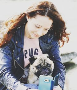 Young woman using phone while sitting with pug on sunny day