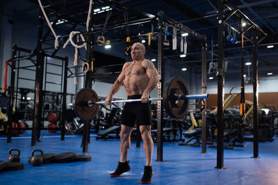 Determined elderly man lifting barbell in contemporary gym