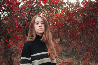 Autumn portrait of a beautiful cute woman against a background of bright red leaves. black sweater