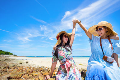 Excited women wearing sunglasses at beach against sky