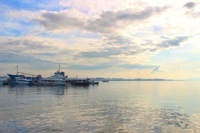 Boats in sea against cloudy sky