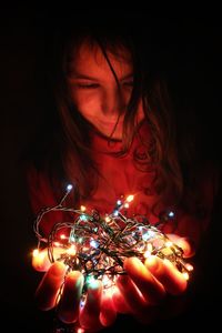 Smiling girl holding illuminated string light in darkroom