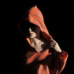 Close-up of young woman wearing hooded shirt against black background