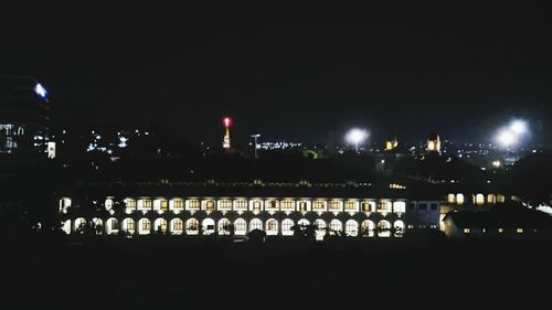 Illuminated buildings by river against sky at night