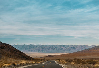 Road leading towards mountains against sky