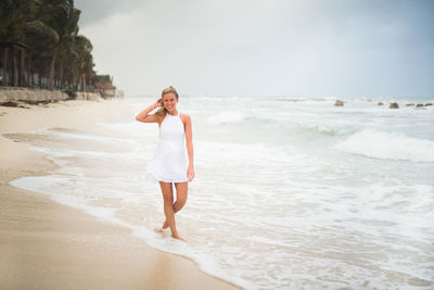 Smiling woman walking at beach against sky