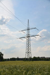 Low angle view of electricity pylon on field against cloudy sky during sunny day
