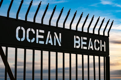 Text on metal fence against sky