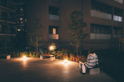 Woman sitting by illuminated building at night