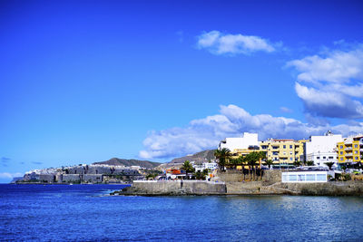 Buildings by sea against blue sky