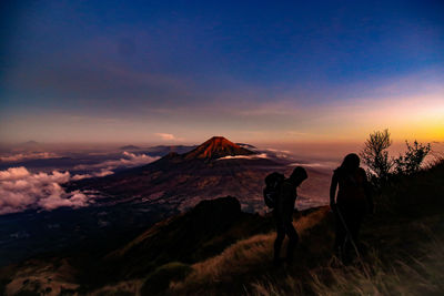 Silhouette people hiking on mountain against sky during sunset